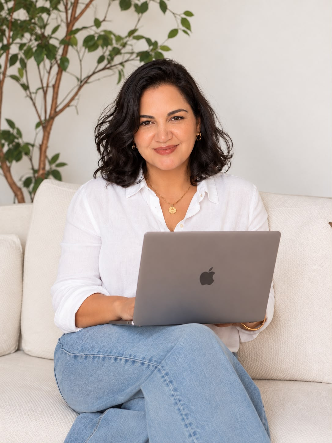 Roberta sentada em um sofá claro, com um notebook no colo, em sala iluminada por luz natural